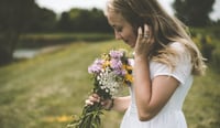 een meisje in een grasveld ruikt aan een boeket wilde bloemen